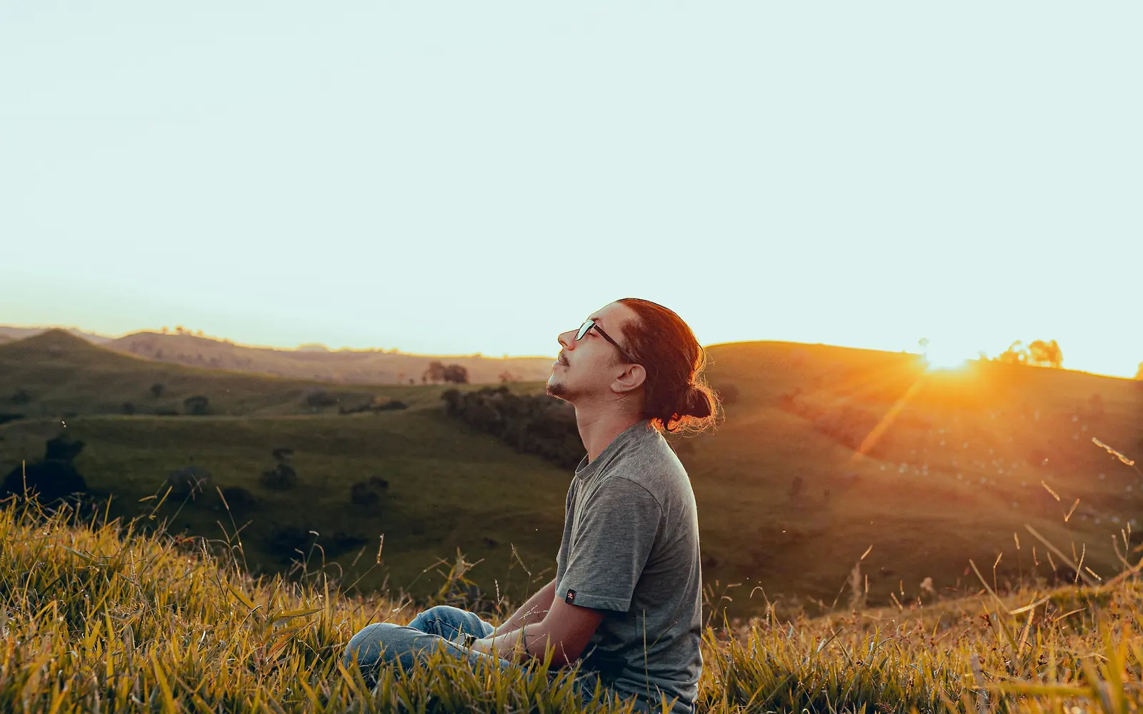 A person sitting in tall grass on a hillside at sunrise
